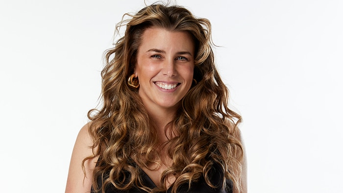 ABC Classic presenter Megan Burslem stands on a white background with a big smile and curly blonde and brown hair.