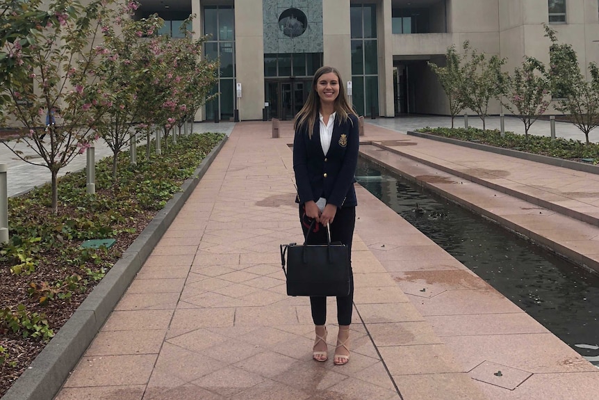 A woman stands in front of Parliament House smiling