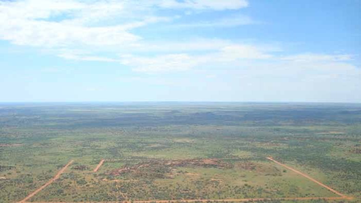 A large expanse of green land with a rectangular boundary under a blue sky with a few white clouds.