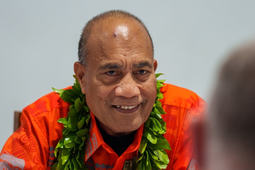 mostly bald older man of pacific islander appearance sitting smiling wearing a lei