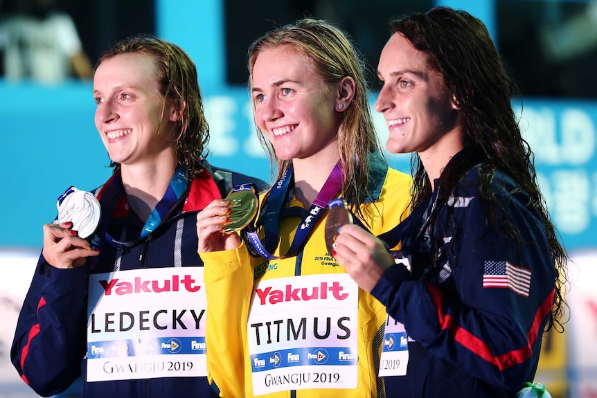 Three women smile and hold their medals, Australia's Ariane Titmus stands in the middle