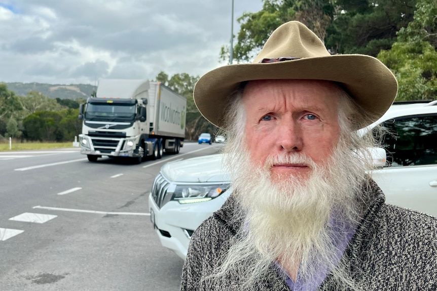 A man with a grey beard stands by a busy road as a truck approaches
