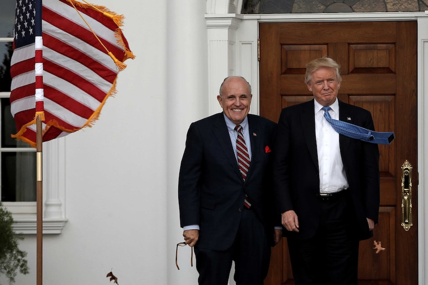 Donald Trump and Rudy Giuliani smiling next to an American flag.