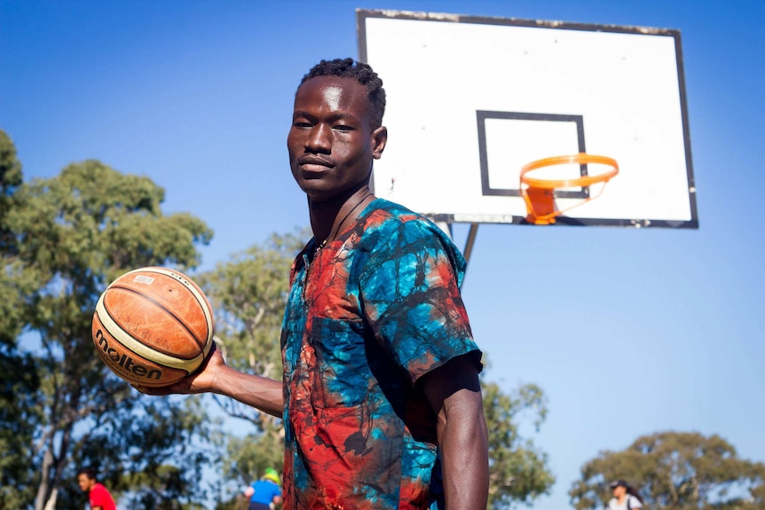 A young man stands in front of a basketball hoop.