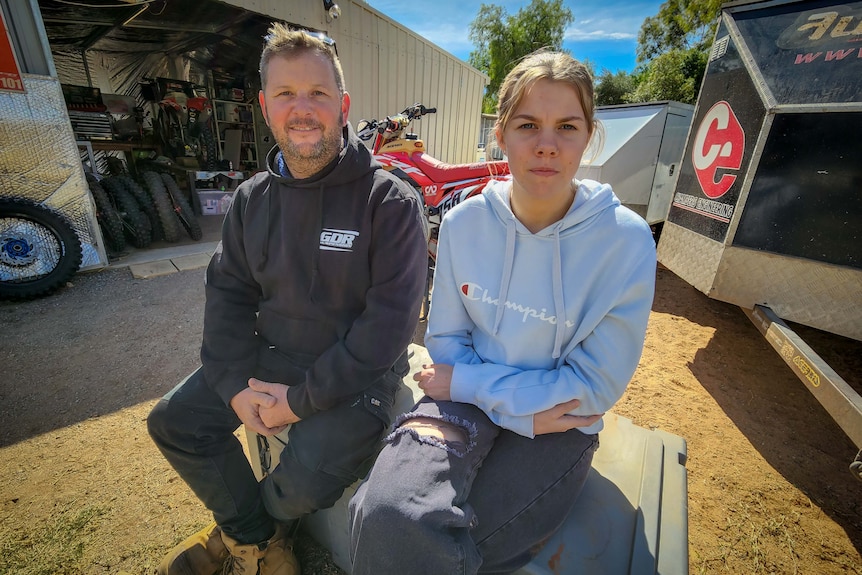 man and 16 yo girl sitting next to each other in backyard, dirt bikes in the background