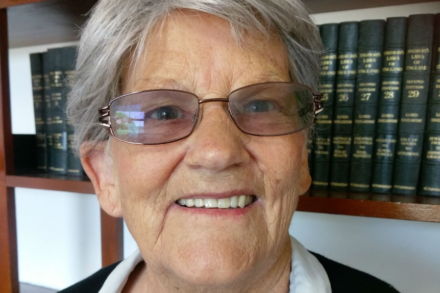 A woman with grey hair and glasses sitting in front of a bookshelf.