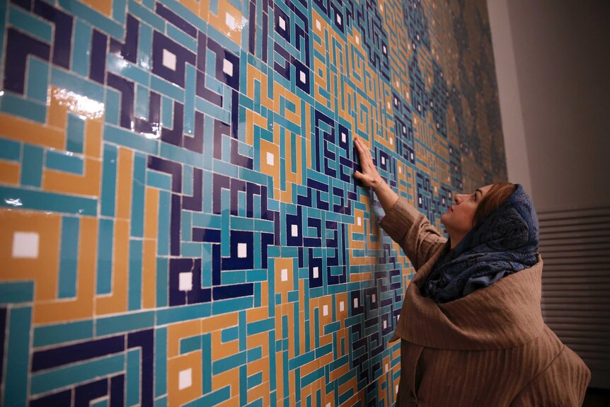 Veiled woman touching coloured tiles featuring modernist design of the mosque's interior wall.