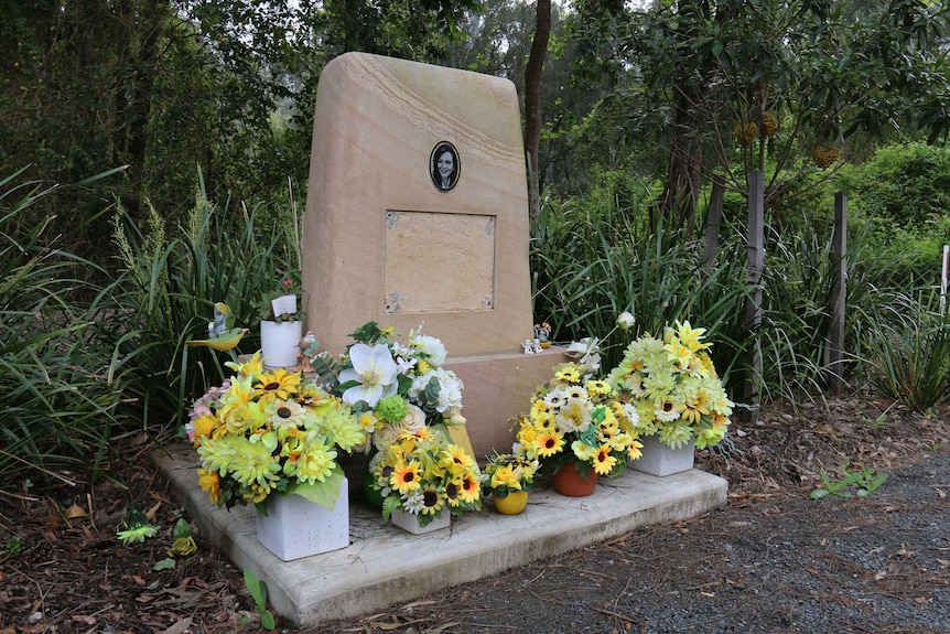 A sandstone memorial with yellow flowers, has its plaque missing.