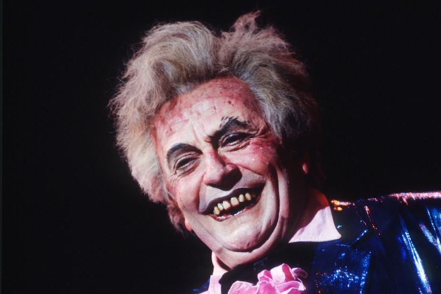 Barry Humphries in character as Les Patterson, who has grey hair and an accentuated grotesque mouth and spotted and pallid skin.