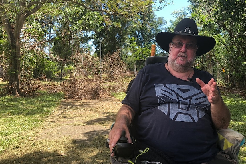 Michael Burge sits in his wheelchair near a footpath with a fallen branch obstructing it.