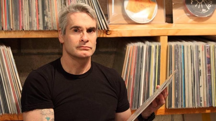 man with grey hair and black t-shirt sitting in front of record collection