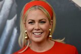 Samantha Armytage looks slightly to the left as she smiles. She wears a red dress, matching headband and gold earrings.