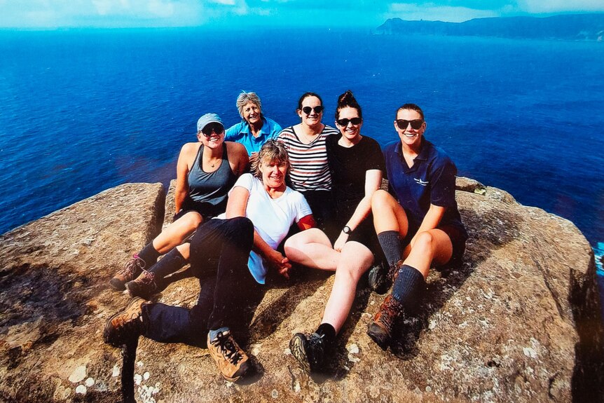A group of female bushwalkers pose on a rock high above a deep blue sea