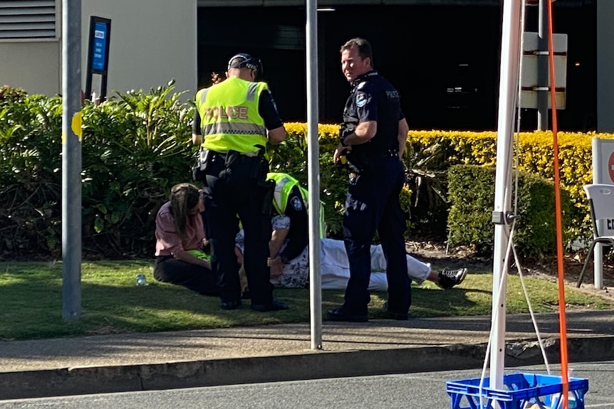 A man, surrounded by police, lying on a grassed area near some hedges.