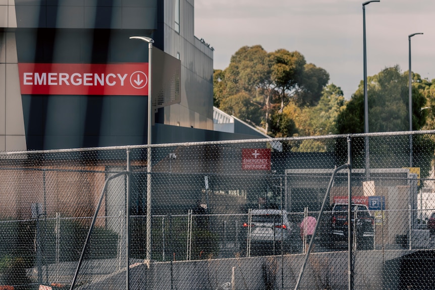 A hospital behind a fence, with an "emergency" sign visible.
