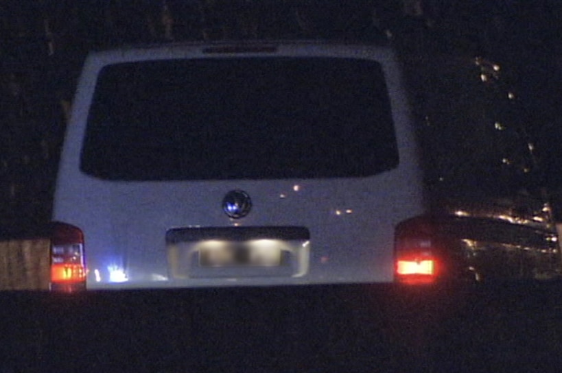 A white van sits stationary in a right-hand lane of the tollway, at night.