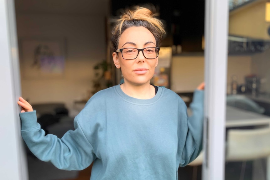 Sarah Goulding, wearing glasses and with her hair up, stands in the doorway of her home.
