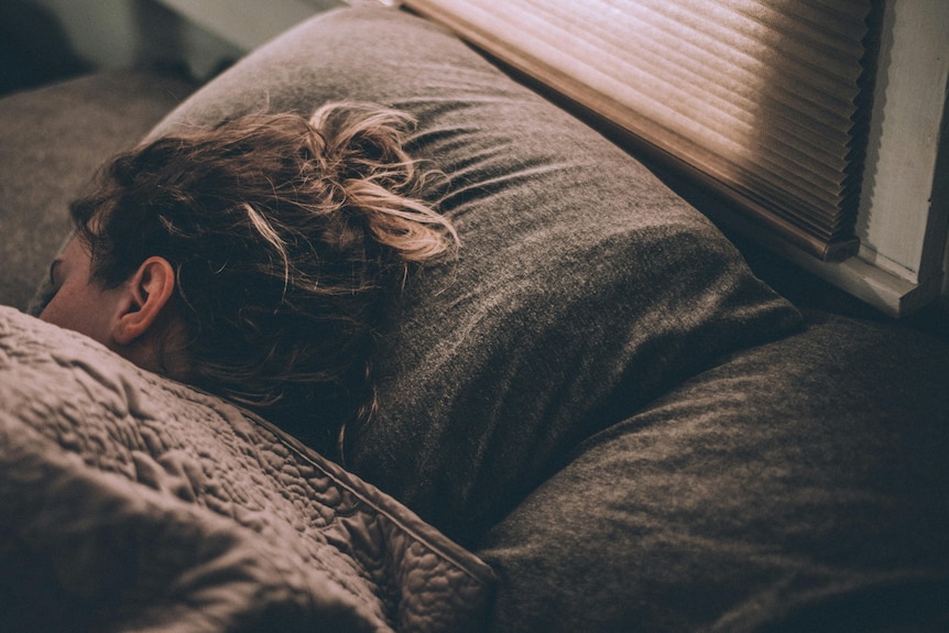 A lady laying in bed with her head on the pillow with a doona covering her body