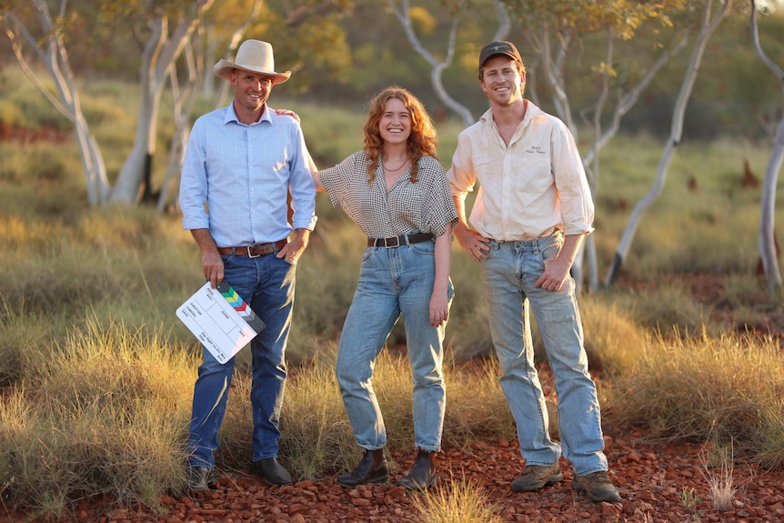 Two men and a woman wearing shirts and jeans in a bush setting