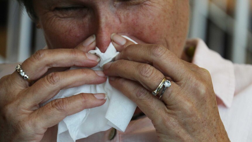 A woman holds a tissue to her nose as she sneezes into it.