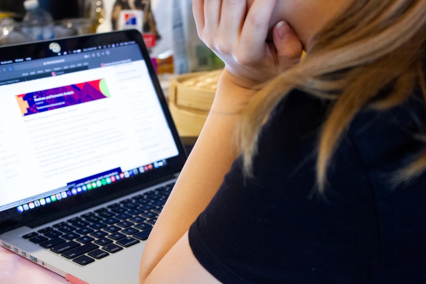 A woman with her face not visible works on a laptop computer.