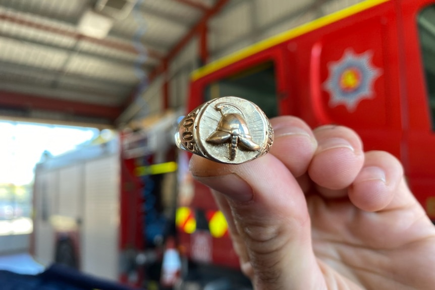 A hand holds a ring embossed with a firefighter's helmet.