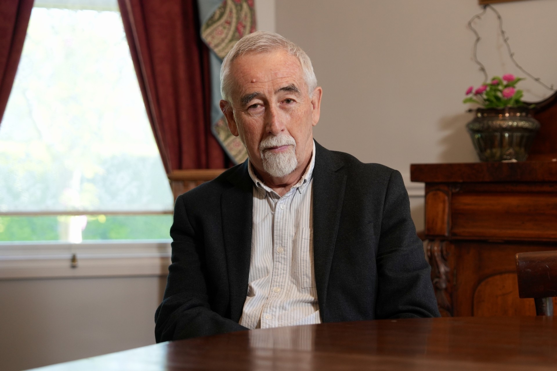 Man in a suit sitting at a table looking into the camera with a neutral expression