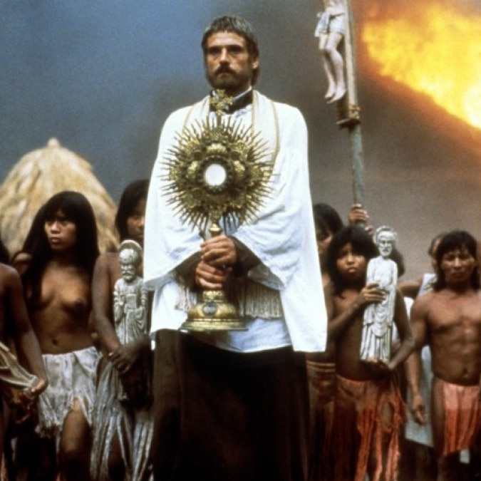 A religious man in white robes surrounded by native peoples