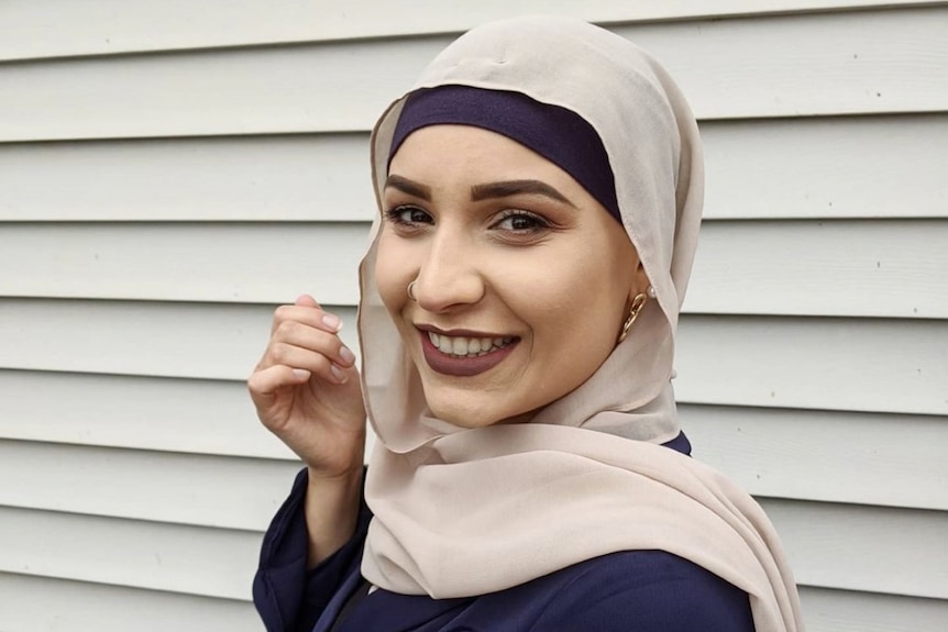 A woman in a blush colored hijab poses for a photo 
