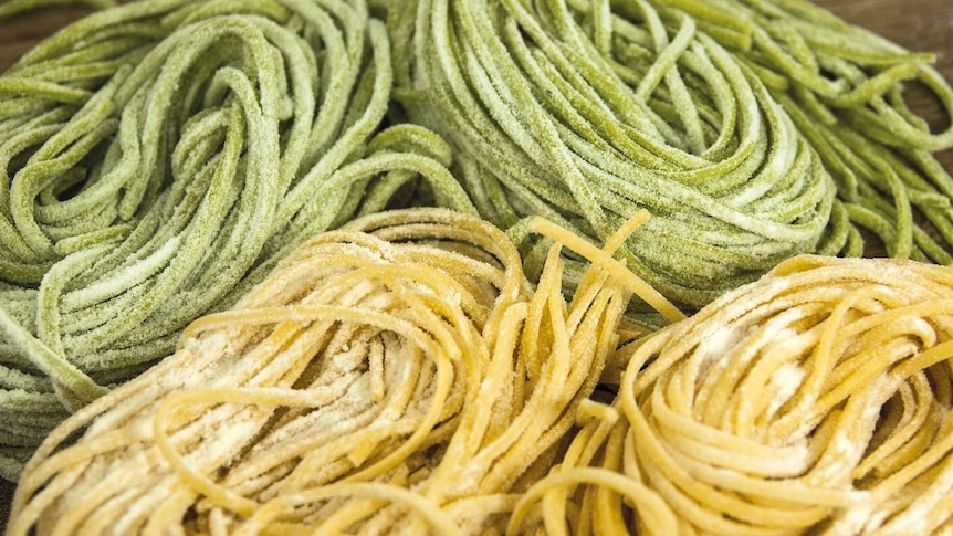Bundles of uncooked spaghetti coloured yellow and green with flour on them