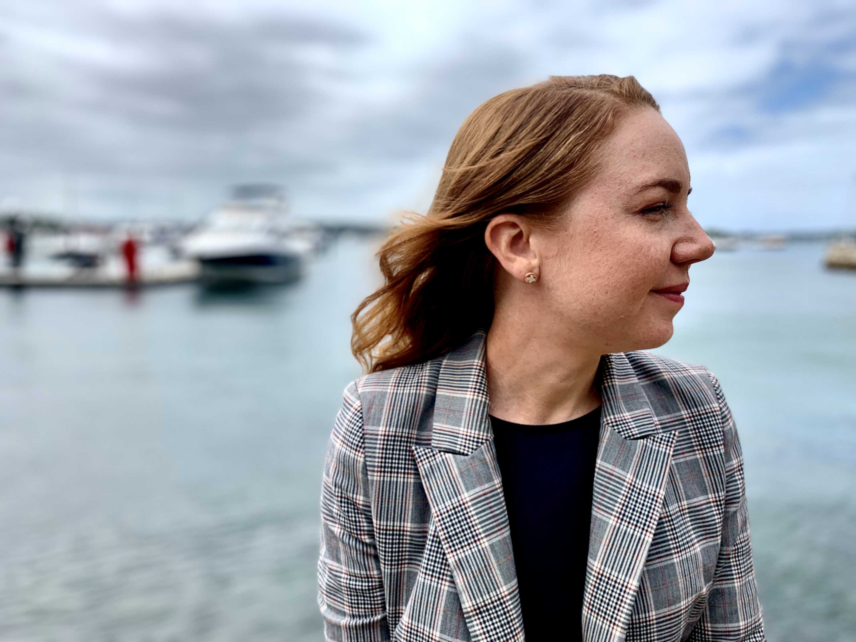 A woman looking side on sits outside near the water somewhere in Sydney.