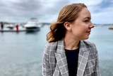 A woman looking side on sits outside near the water somewhere in Sydney.