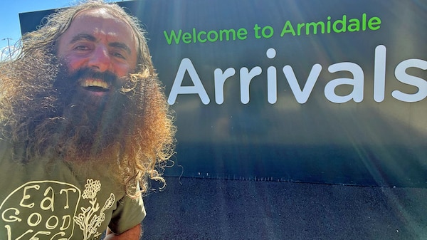 Costa standing in front of a sign saying 'Welcome to Armidale' Arrivals.