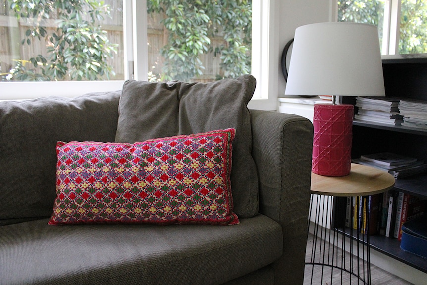 A hot pink embroidered cushion sitting on a grey couch next to a hot pink lamp on a side table.