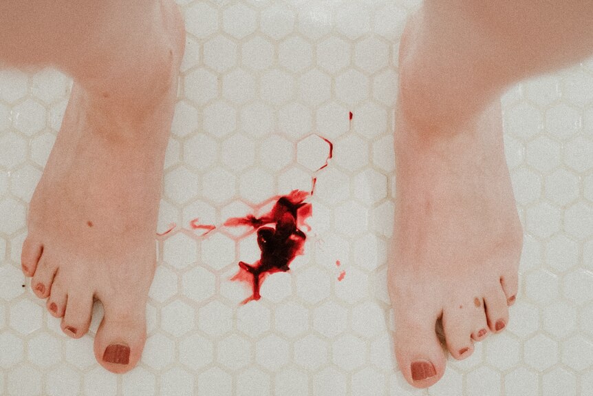 A red liquid that appears to be blood on the floor between someone's feet.