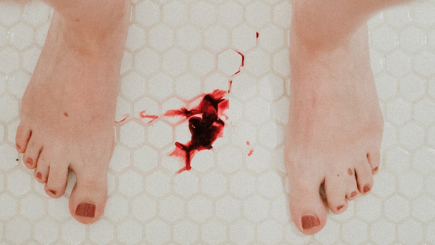 A red liquid that appears to be blood on the floor between someone's feet.