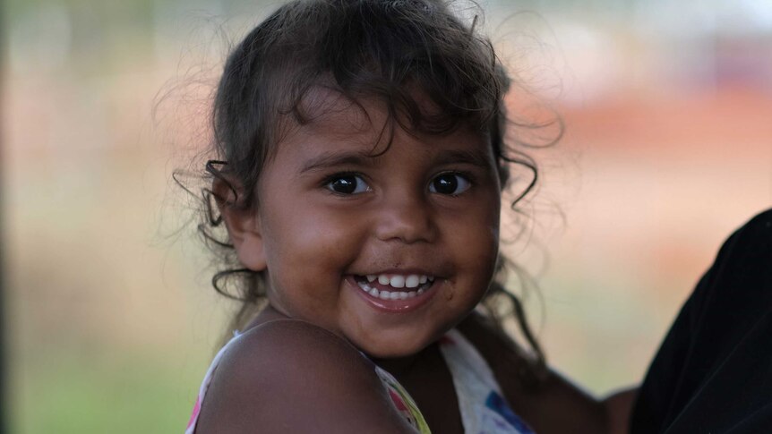 A young Indigenous girl with curly hair and bright eyes smiles for the camera.