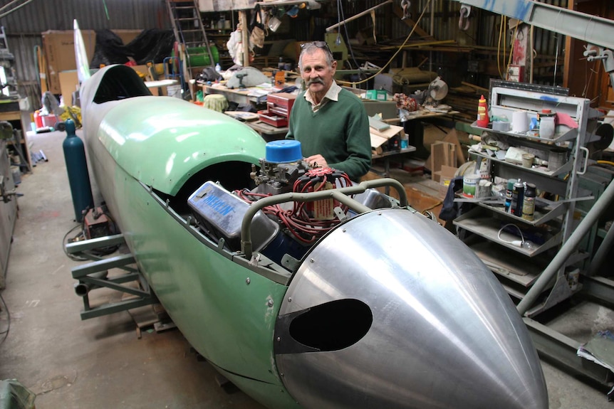 Rod McNeill stands at the side of the spitfire aeroplane he is constructing.
