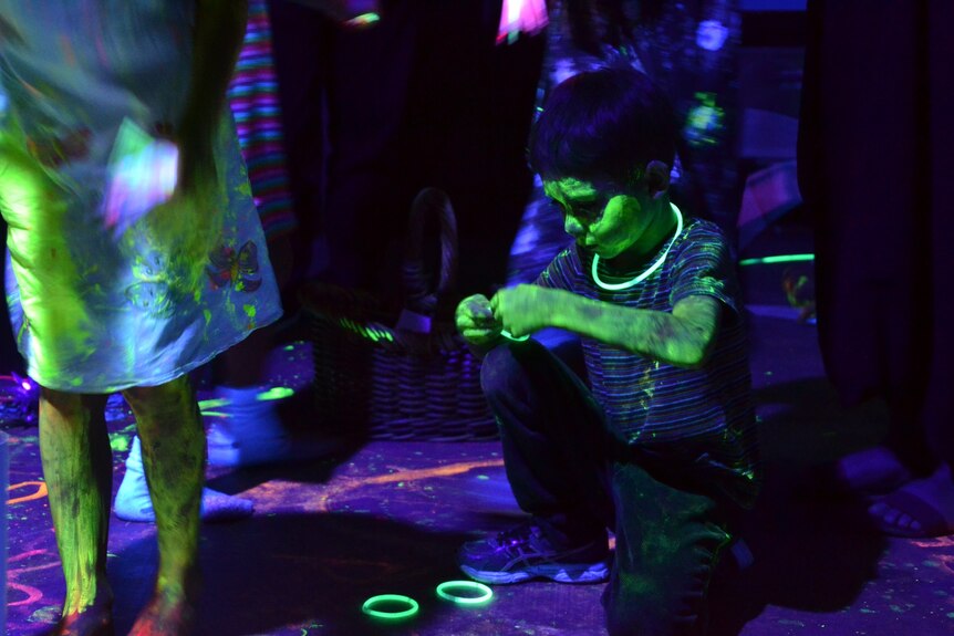 Myles Scharf plays with glowsticks on the ground during his father Julian's party.