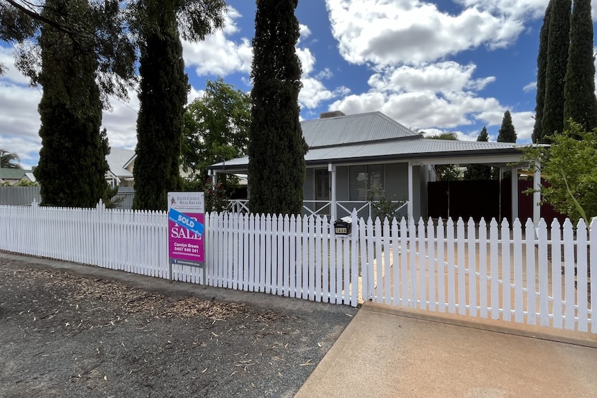 a pink for sale sign in front of a house with a white picket fence 