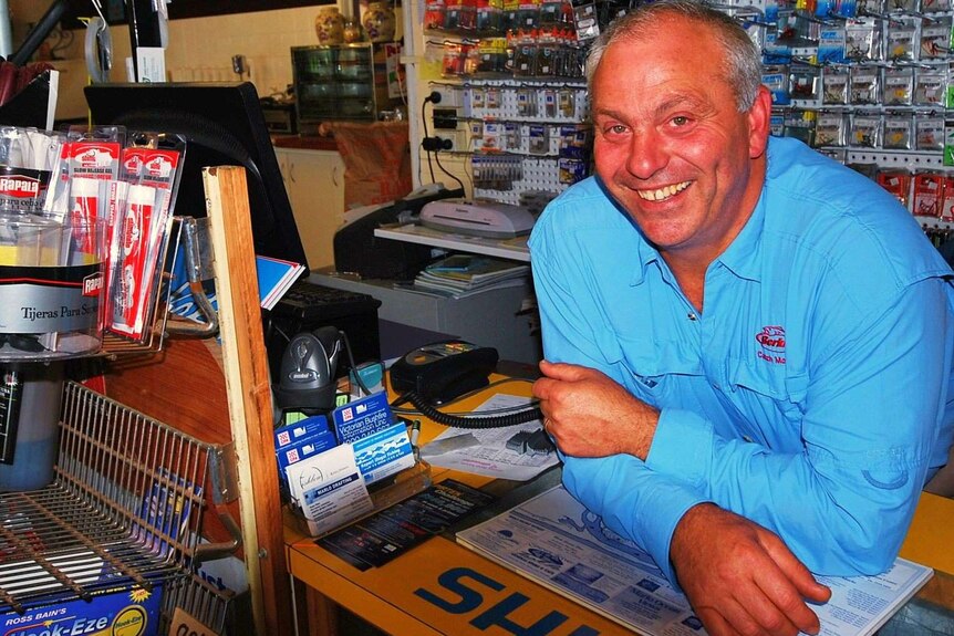 Dave Ballinger leans on the counter of his Snowy River Tackle shop, surrounded by fishing equipment