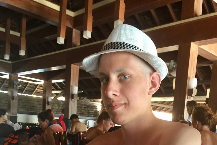 A teenage boy in a fedora sits at a table.