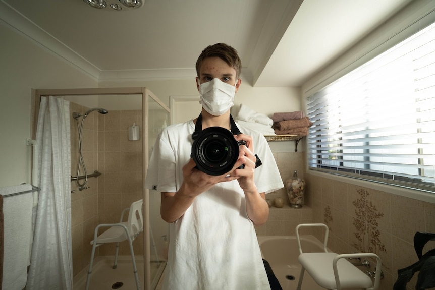A young man wearing facemask and gown holding a camera