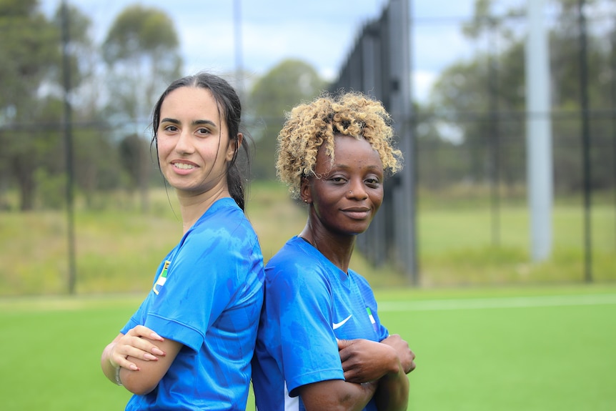 Two women stand back to back, arms crossed, smiling at the camera.