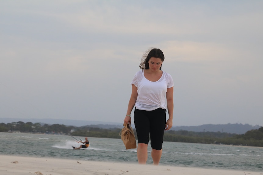 Paris looks down as she walks along the beach carrying a bag, in an old supplied photograph.