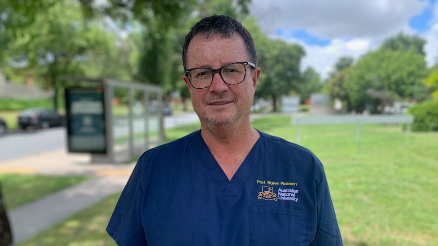 A man in blue medical scrubs smiles at the camera.