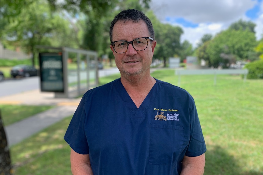 A man in blue medical scrubs smiles at the camera.