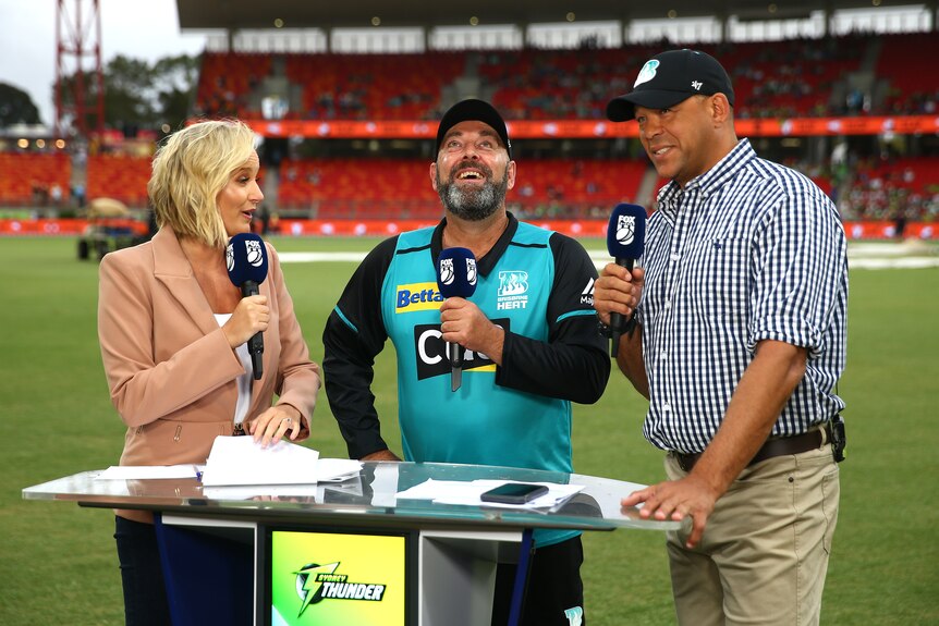 Andrew Symonds holds a microhphone alongside Darren Lehmann and Jessica Yates