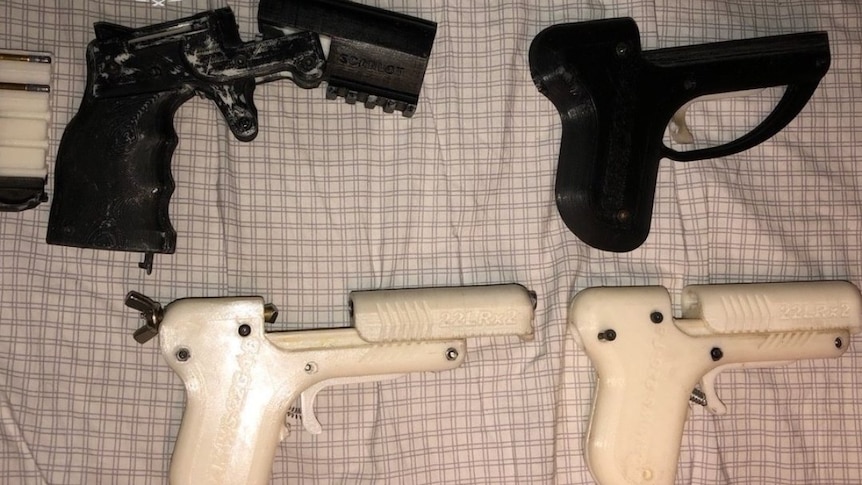 Four 3D printed guns laid out on a bed. 