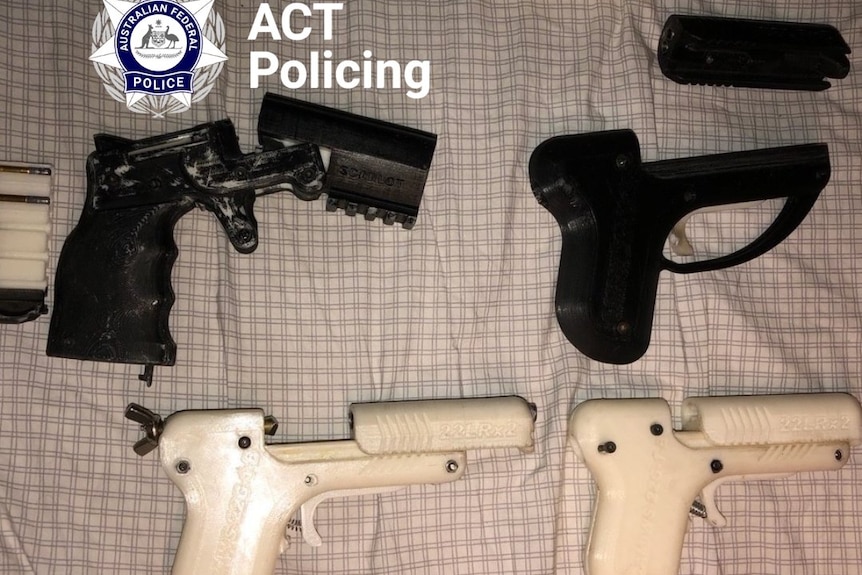 Four 3D printed guns laid out on a bed. 